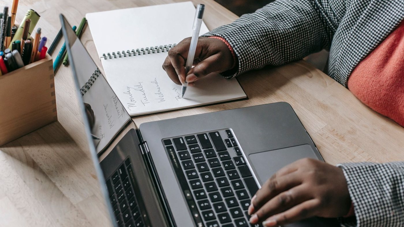Person planning a client process in a notebook beside a laptop